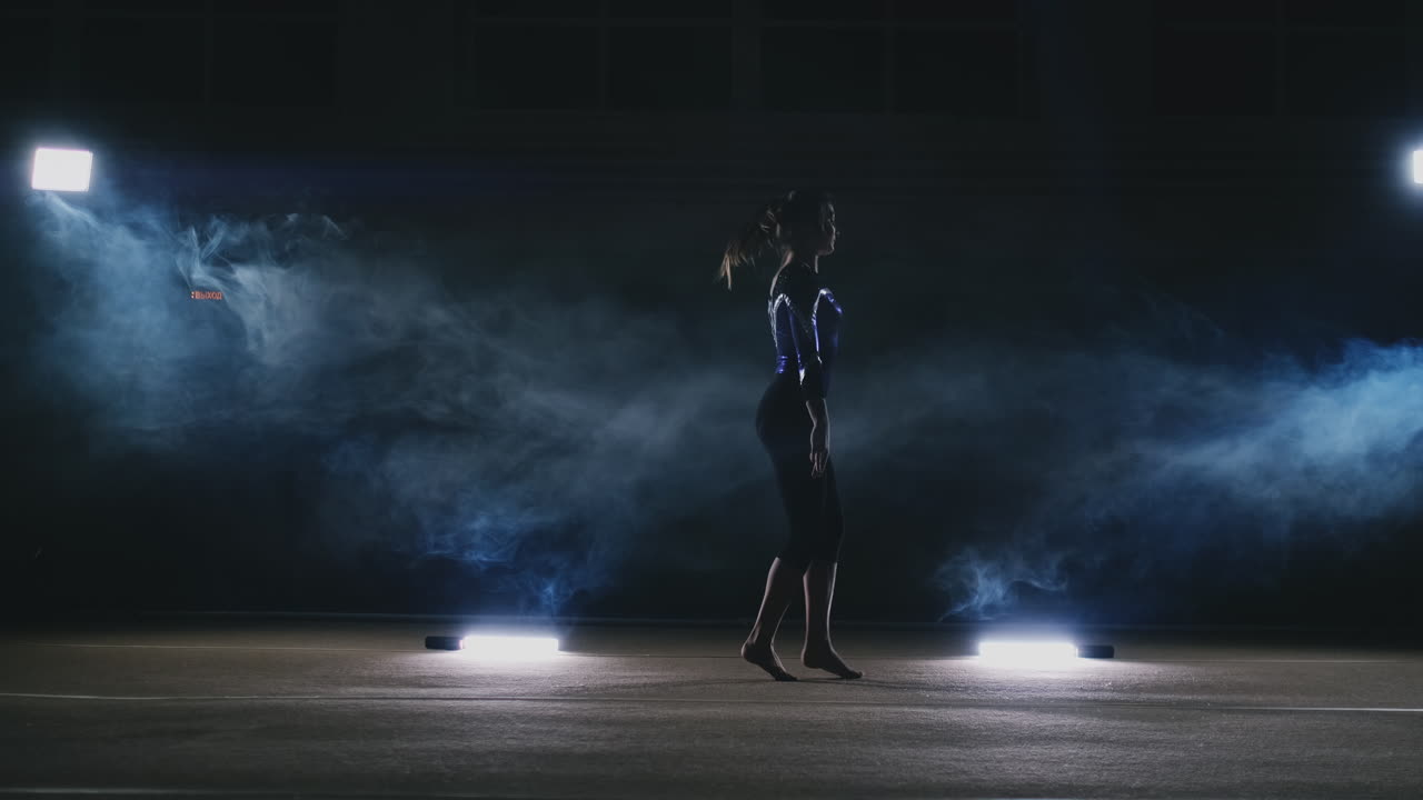 In slow motion in the smoke girl acrobat performs several back flips and coups in the air. Training acrobatic performance. Women's gymnastics competitions.