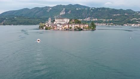 isola san giulio on lake orta, italy with a boat passing by, green hills in the background, aerial view