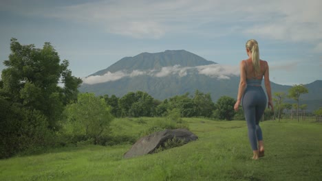 serene blond woman walking towards boulder to get a better look at volcano agung