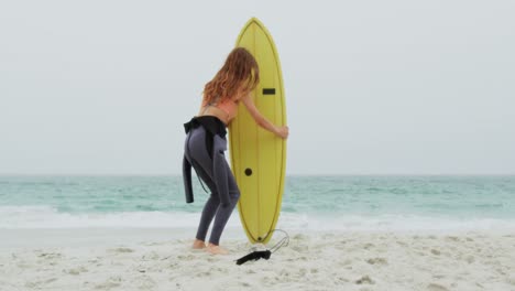 rear view of caucasian female surfer standing with surfboard on the beach 4k