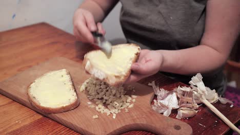 Frauenhände-Buttern-Eine-Scheibe-Brot,-Der-Gehackte-Knoblauch-Liegt-Auf-Einem-Schneidebrett