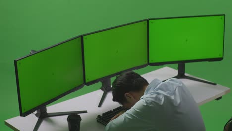 vista lateral de un hombre asiático cansado durmiendo mientras trabaja con un simulacro de varios monitores de computadora en un estudio de pantalla verde