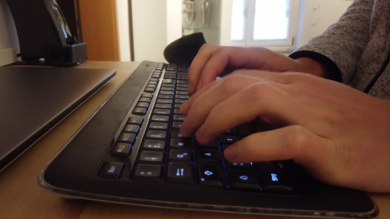 Caucasian man is typing on a black LED lit keyboard and mouse