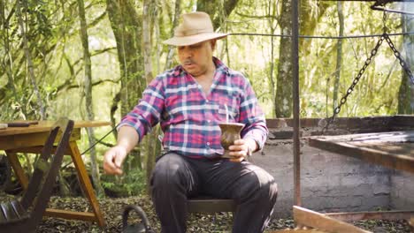 Ethnic-man-serving-mate-against-barbecue-rack-in-garden