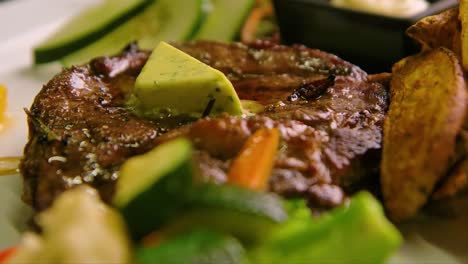 Slow-dolly-and-focus-rack-of-plate-with-steak-topped-with-garlic-butter,-grilled-vegetables-and-potatoes