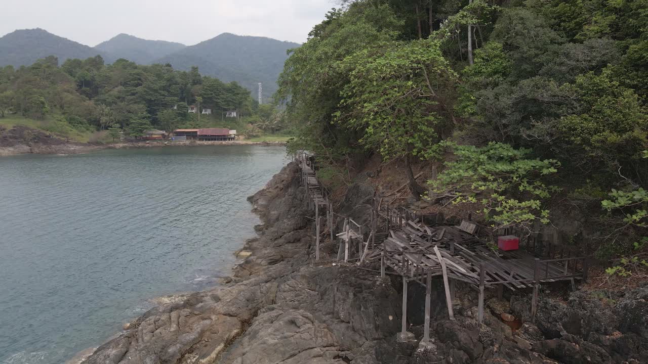 el dron dejó una toma de camión de una plataforma de madera y una pasarela que se está derrumbando en la costa de rocas de granito en una isla tropical con un exuberante bosque verde y un océano