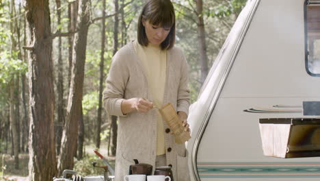 lächelnde frau, die auf dem campingplatz im wald kaffee kocht