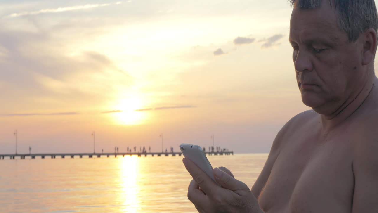hombre con teléfono inteligente junto al mar al atardecer