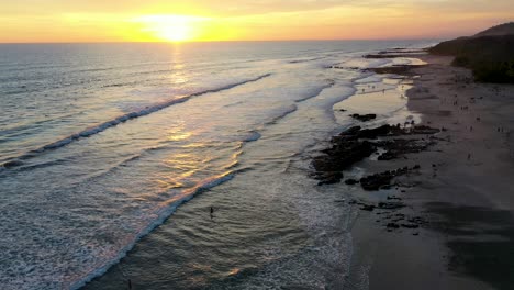 aerial flying across sunset reflecting in the water with waves and surfers in the pacific ocean in tamarindo, costa rica