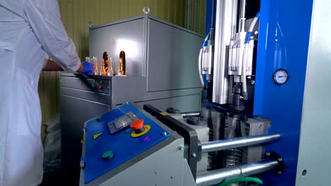 un trabajador con una bata de laboratorio hace preformas en grandes botellas para mascotas.