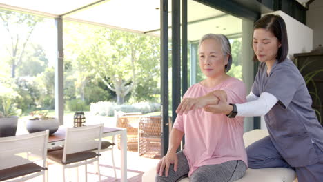 physiotherapist assisting senior asian woman with arm exercises at home therapy session