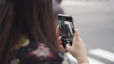 female tourist taking photos of times square with her smartphone on crosswalk.  new york usa