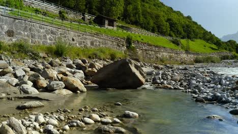 Aerial-drone-flyback-view-at-low-altitude-over-Mera-river-water-surface-and-rocks-and-under-bridge