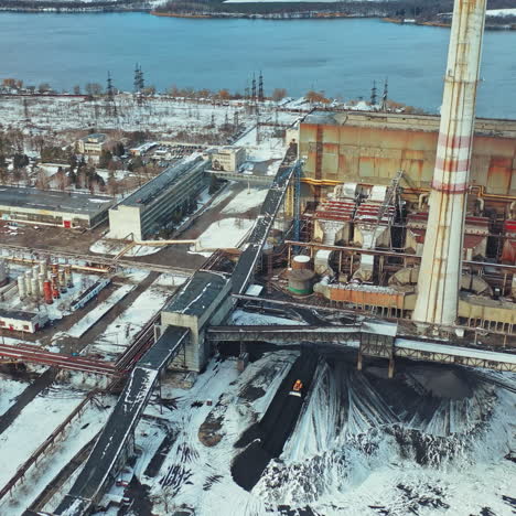 aerial view of the vast territory of the thermal power station with administrative buildings, workshops and heaps of ash from coal, which excavator levels on the background of river behind of it.
