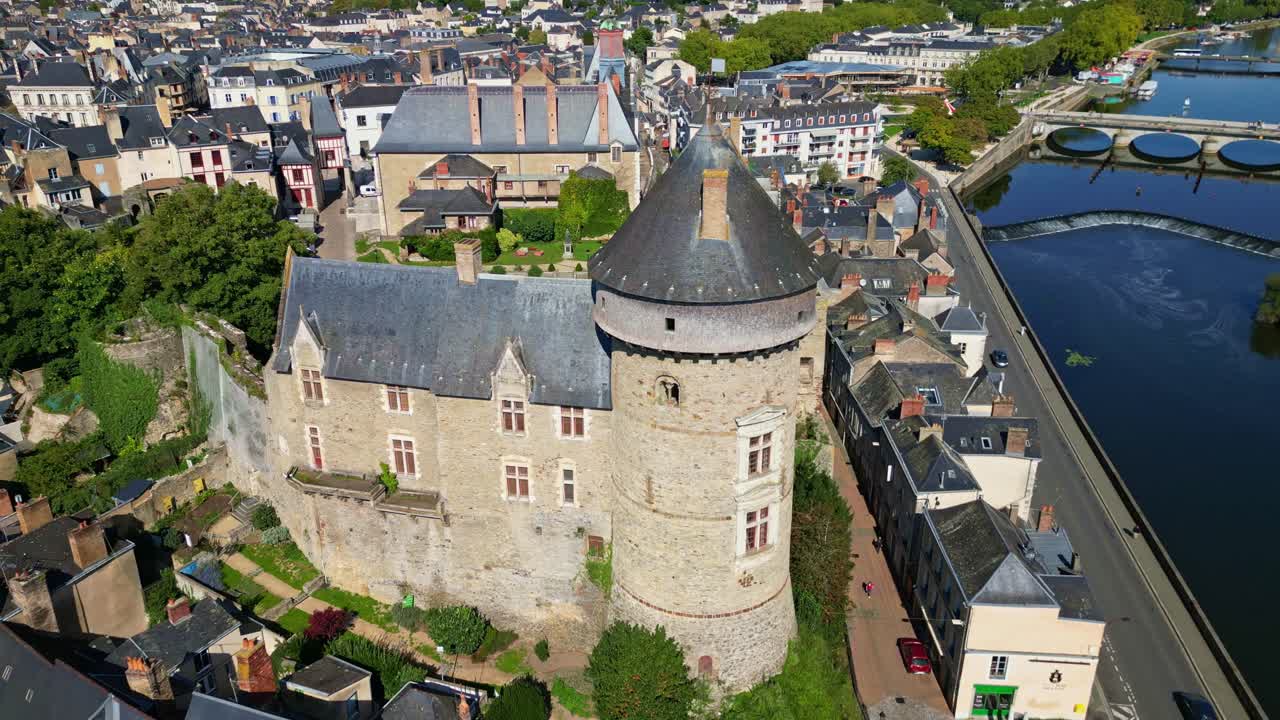 Drone flying backward over Laval Castle showing river, bridge, and city streets on sunny day