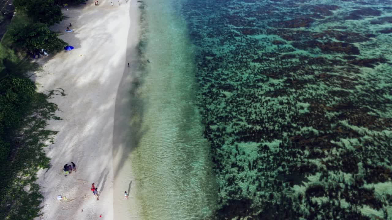 Aerial view of St. Felix Public Beach in Mauritius reveals white sand, turquoise shallows, and reef textures. A tranquil moment with a few people enjoying the peaceful shoreline.