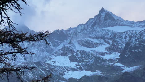 Swiss-alps-autumn-first-snow-dusting-mountain-peaks-Saas-Fee-Zermatt-Saastal-alpine-valley-chalet-ski-resort-town-sunset-orange-pink-high-clouds-Switzerland-Europe-Lark-tree-wind-static-shot