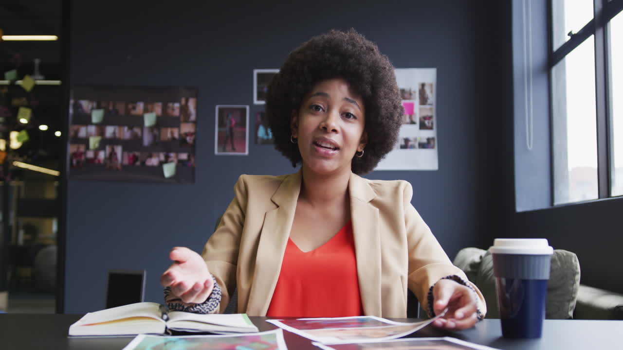 Biracial businesswoman sitting having a video chat going through paperwork in a modern office