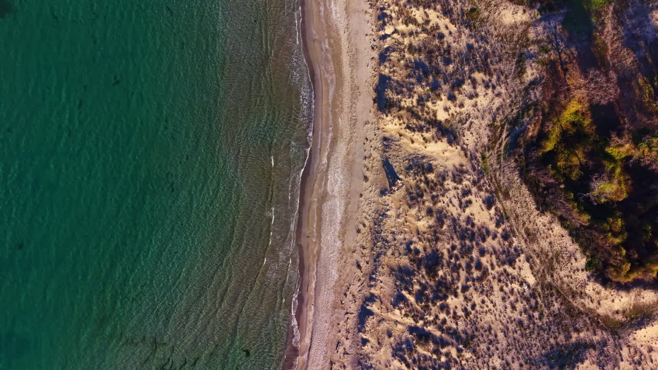 Vibrerende turkisblåt vand slår blidt ind mod en gylden sandstrand omkranset af frodig grøn beplantning under den strålende sol i et fredfyldt kystparadis.