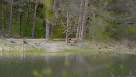 A-man-in-a-red-hoodie-is-resting-on-a-bench-by-the-lake