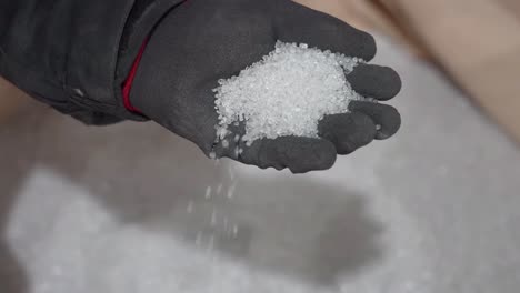 close up shot, a gloved hand holding a pile of white powder. the powder is falling from the hand onto a surface.