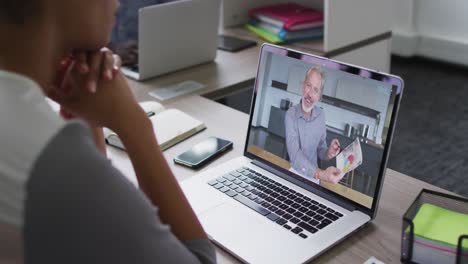 mujer afroamericana teniendo una videoconferencia en una computadora portátil con un colega de oficina masculino en la oficina