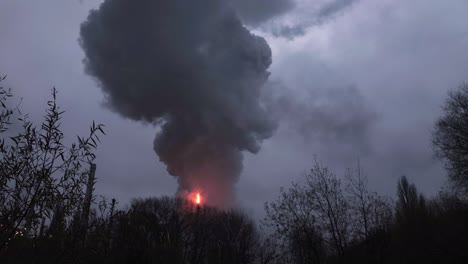 incendio industrial de una chimenea que genera humo negro caliente empujado al aire en un día gris nublado