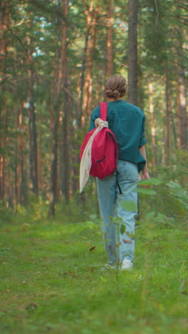vista de atrás de un excursionista caminando lentamente a través de un sereno bosque iluminado por el sol, una mochila roja colgada sobre su hombro, parece cansada, ajustando la posición de la mano en la mochila