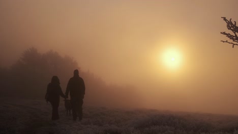 silhouette of a couple with dog in a iced winter landscape during a storm with high wind at sunset