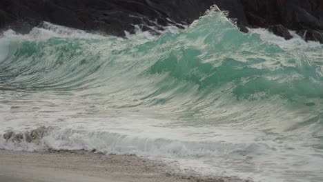 powerful waves are crashing on the rocks and spilling on the sandy beach