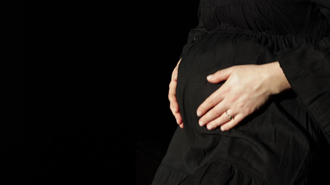 Close-up of an expectant mother's pregnant belly as she massages it with her hands.