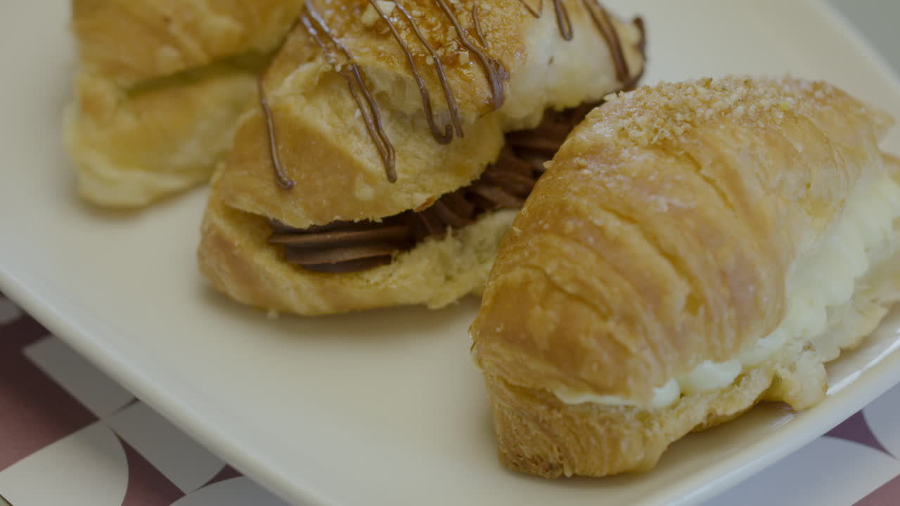 Primo piano di tre croissant di pasta sfoglia ripieni di crema, presentati su un piatto bianco