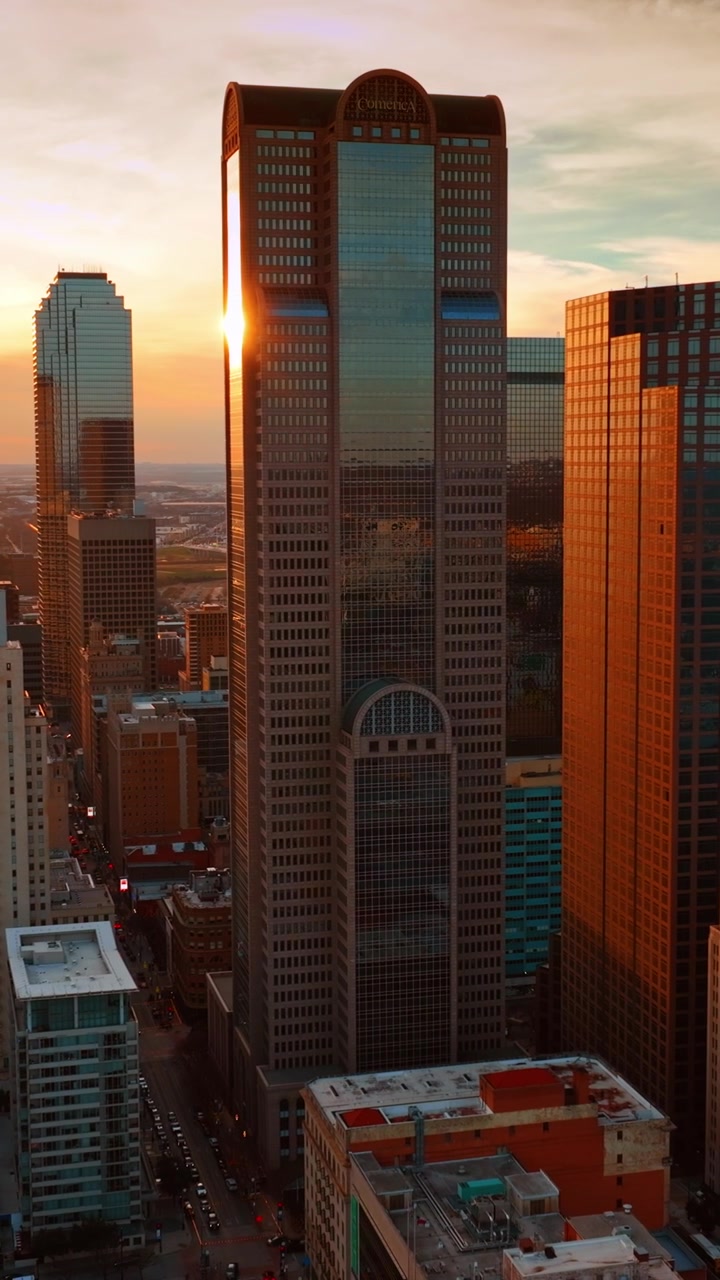 Luz alaranjada cobrindo as fachadas dos belos arranha-céus do centro de Dallas. Vista da cidade ao pôr do sol do alto. Vídeo vertical