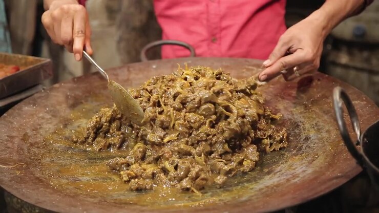 Venditore ambulante che cucina mutton masala su una grande padella calda nella vivace Shivajinagar, Bangalore.