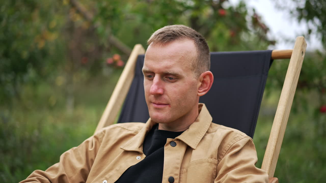 Mid aged Caucasian man focused on the work on his laptop. Male freelancer working remote in nature. Lady at backdrop speaking on the phone.