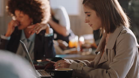 Junge-Frau-Benutzt-Laptop,-Arbeitet-Im-Café-Und-Tippt-E-Mails,-Teilt-Nachrichten-Auf-Smartphone-Social-Media-Kanälen-Und-Genießt-Es,-In-Einem-Belebten-Restaurant-Zu-Sitzen-Und-Kaffee-Zu-Trinken