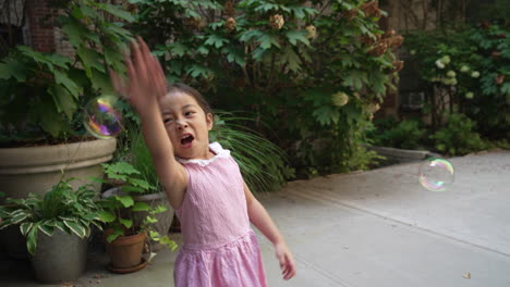 asian girl popping, playing and having fun with bubbles and wearing a pink dress, outside