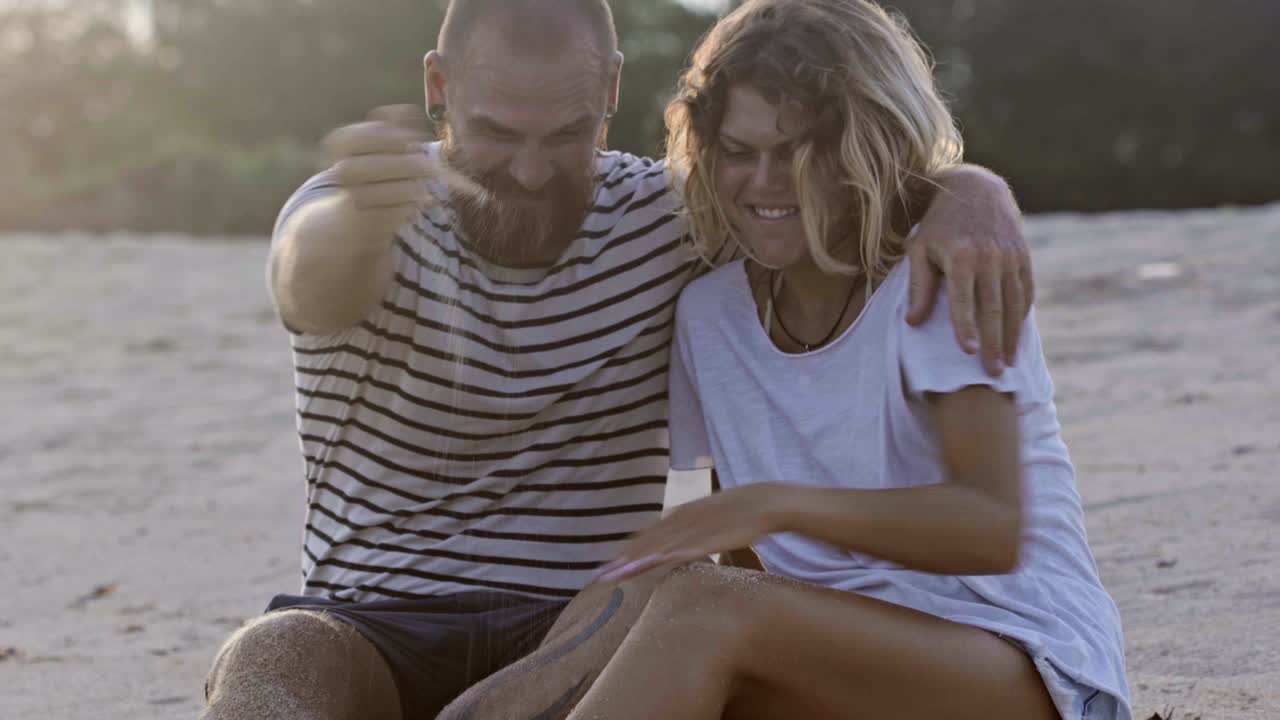 una pareja feliz jugando con arena en la playa.
