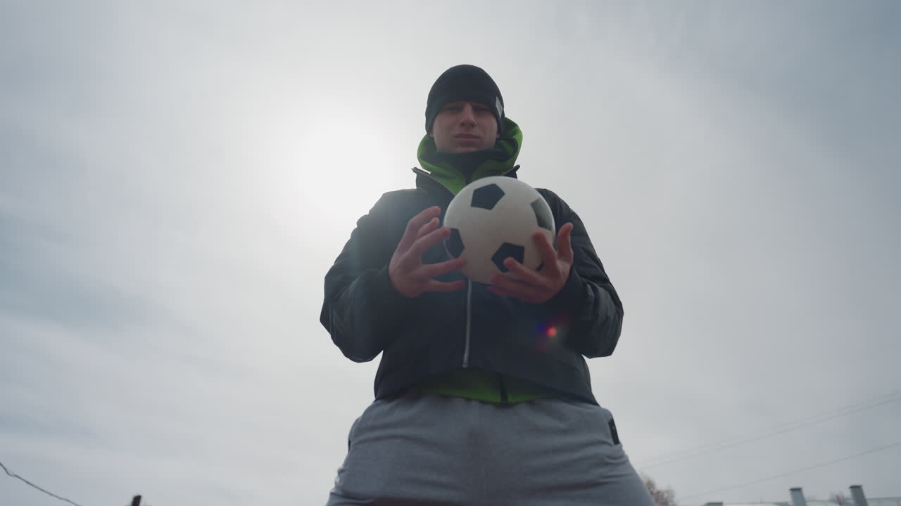 햇볕 아래 야외 훈련 세션에 참여한 밝은 피부의 운동선수, 햇빛 아래 야외에서 축구를 연습하는 자신감 넘치는 남자 운동선수, 햇빛 아래 야외 연습 중 축구공을 들고 있는 자신감 있는 남자의 모습