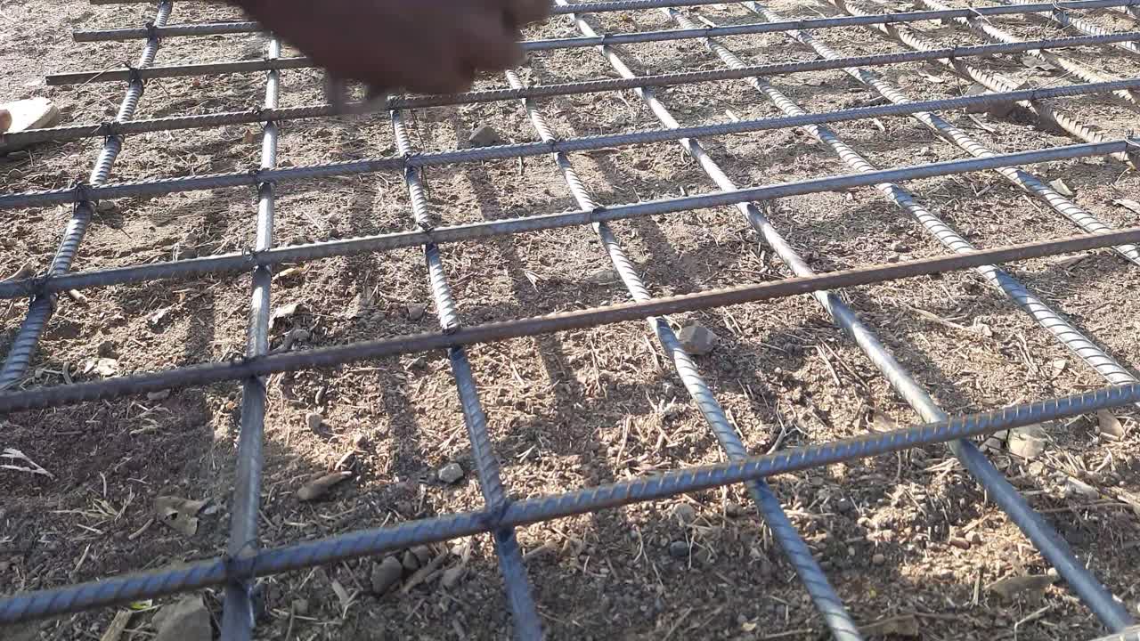 The worker`s hand tying reinforcing steel bars, tightening wire on rebar using pincers for formwork construction. 
Construction rebar steelwork reinforcement. Reinforcements steel bars stack