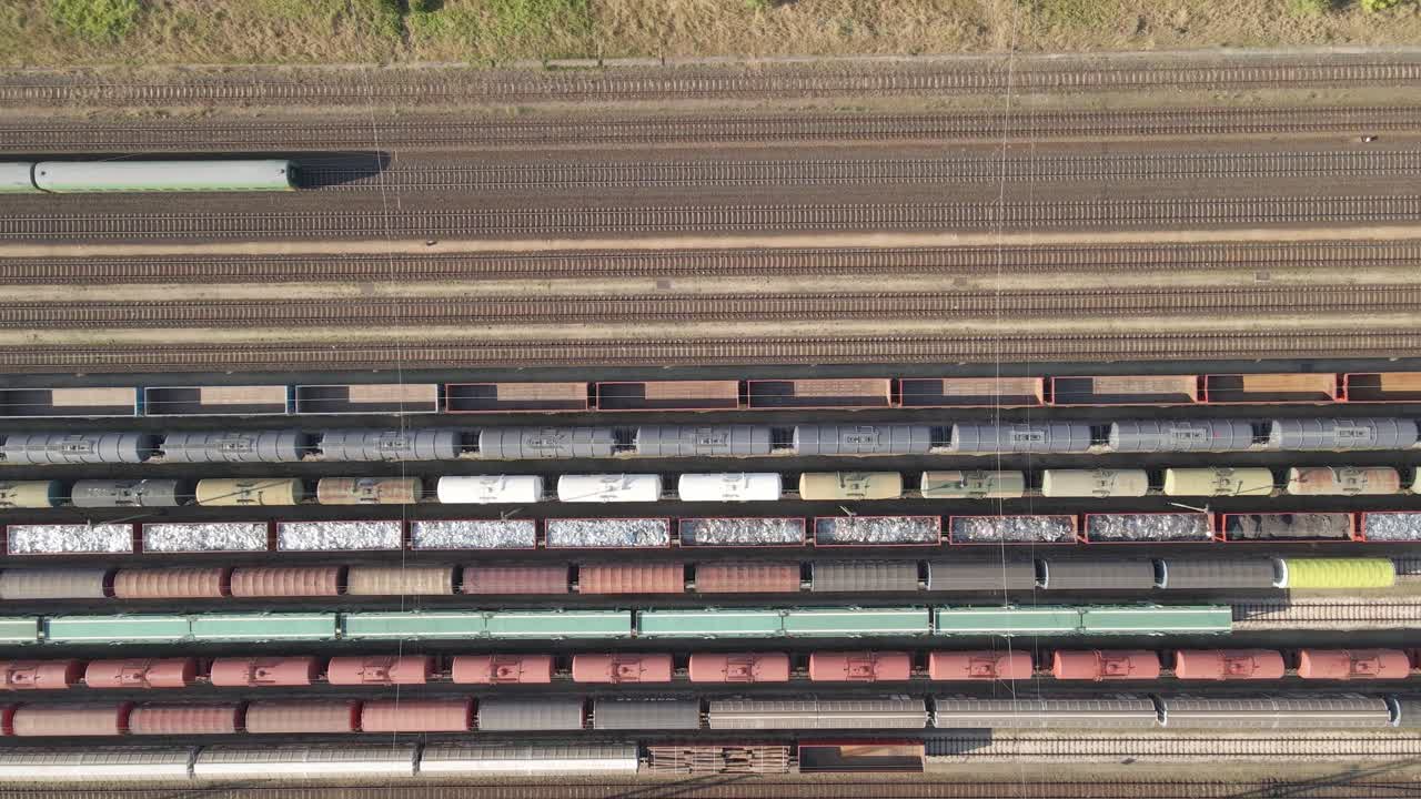 An aerial video of a large railway station shows multiple freight trains on parallel tracks while a passenger train passes through.