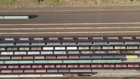 an aerial video of a large railway station shows multiple freight trains on parallel tracks while a passenger train passes through.