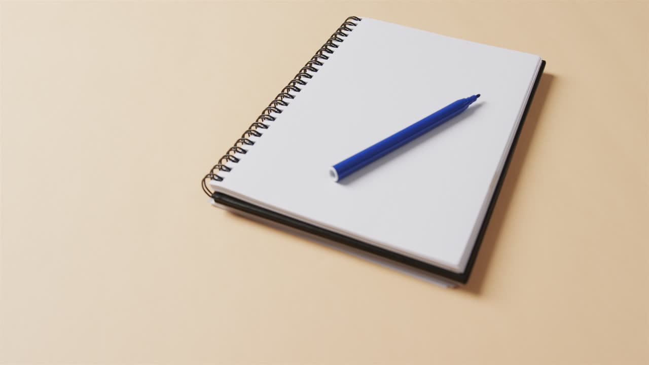 Close up of blue marker on notebook with beige background, in slow motion