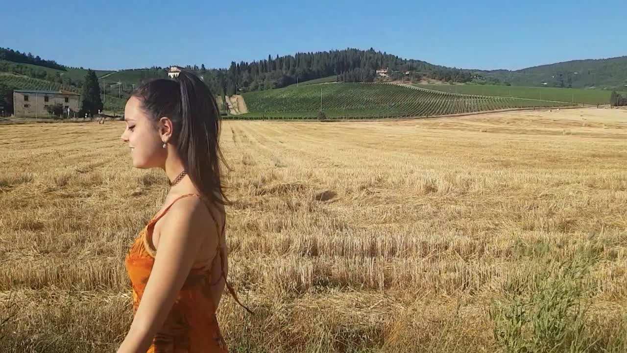 joven morena caminando cerca de un campo de trigo a principios de verano mientras canta