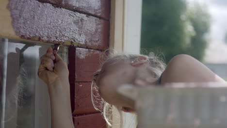 close-up of beautiful blonde girl painting a red traditional finish house, nordic woman doing maintenance work, finland, scandinavia