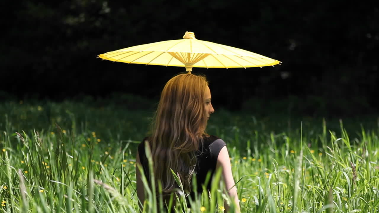 우산을 쓴 여자가 들판에 앉아 있다