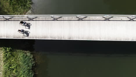 aerial shot top down of two women biking over a bridge ata river with a lot of green trees