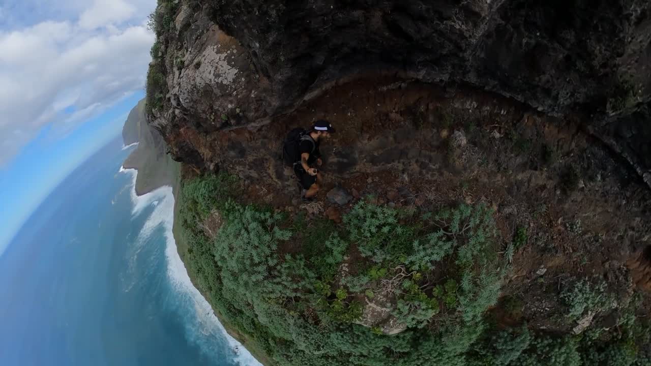 A fit and young man is hiking alone on the narrow path next to the steep edge in Quebrada do Negro in Madeira