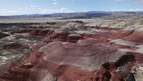 People-on-top-of-colorful-mountains-in-Bentonite-Hills,-Utah,-USA---Orbit,-drone-shot