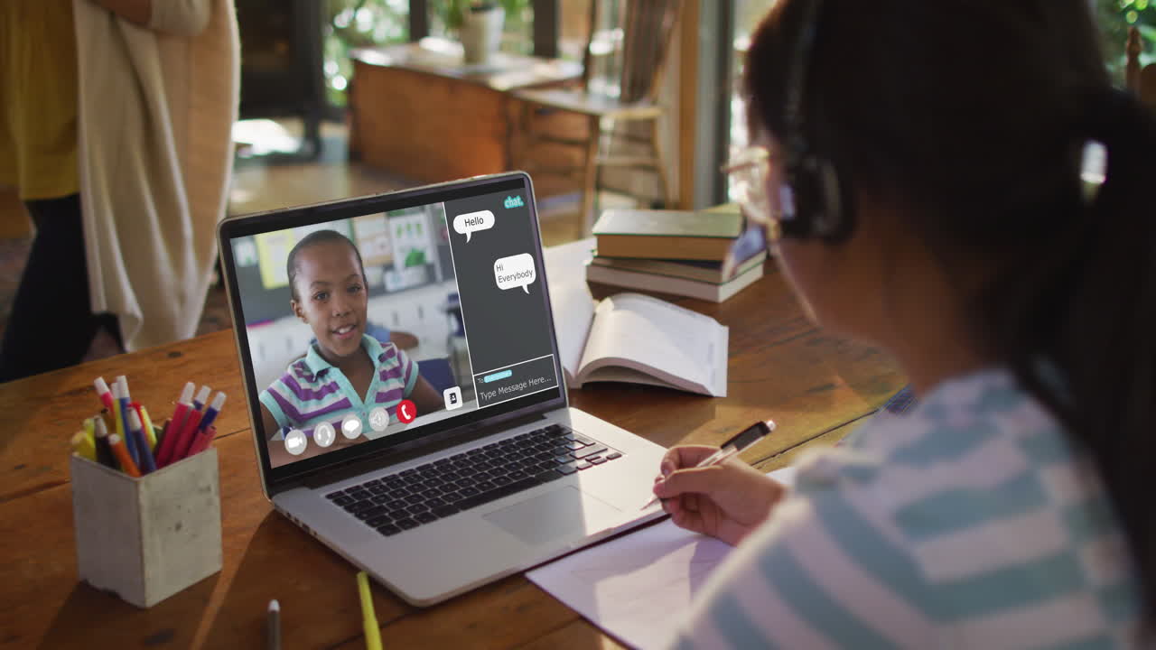 African american girl doing homework and having a video call with classmate on laptop at home